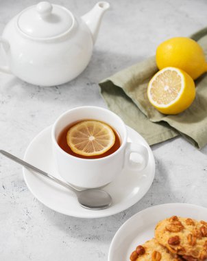Limonlu bir fincan çay ve arka planda ev yapımı kurabiyeler. Beyaz çaydanlık ve narenciye de yakın. Sağlıklı sabah içkisi konsepti. Üst görünüm.