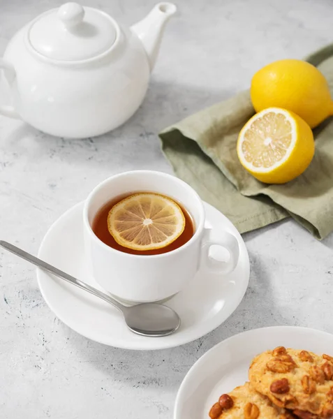 stock image A  cup of tea with lemon and homemade cookies on a light background with a white teapot and citrus close up. Healthy morning drink concept. Top view.