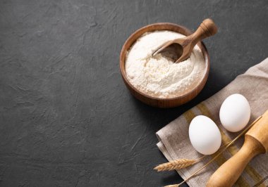 Koyu gri arka planda pişirme, buğday unu, yumurta, merdane ve mutfak tekstili için organik malzemeler. Ev yapımı sağlıklı yemekler.