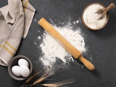 Koyu gri arka planda pişirme, buğday unu, yumurta, merdane ve mutfak tekstili için organik malzemeler. Ev yapımı sağlıklı yemekler.