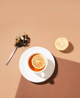 Kahverengi arka planda koyu gölgeli limonlu bir fincan çay. Yiyecek ve içecek konsepti. Üst görünüm ve kopyalama alanı.