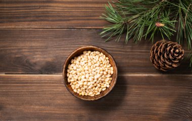 Kahverengi ahşap arka planda çam fıstığı ve çam iğnesi dalları. Sağlıklı beslenme atıştırması. Üst görünüm ve kopyalama alanı.