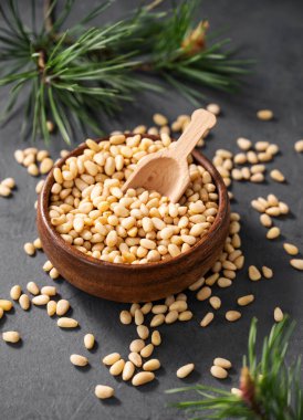 Ahşap bir kasede kepçeyle çam fıstığı ve çam iğnelerinin dallarıyla karanlık bir arka planda serpiştirilmiş. Doğal, organik ve sağlıklı abur cubur kavramı. Üst görünüm.