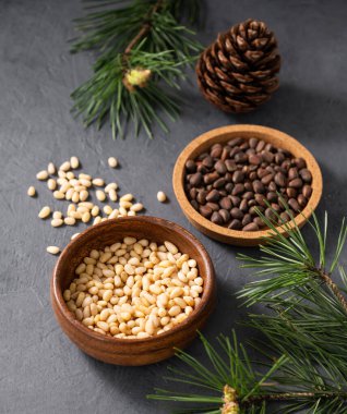 Ahşap bir kasede çam fıstığı ve çam iğnesi dalları ile karanlık bir arka plana serpilmiş. Doğal, organik ve sağlıklı abur cubur kavramı. Üst görünüm.