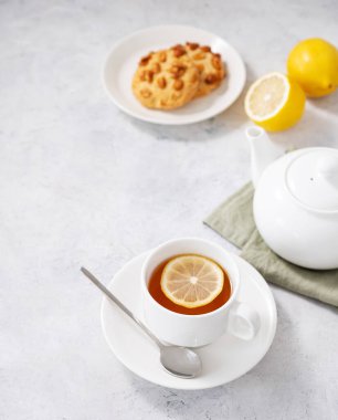 Limonlu bir fincan bitki çayı, kurabiye ve hafif arkaplanda çaydanlık. Sağlıklı ve detoks içeceği konsepti. Metin için boş alan.