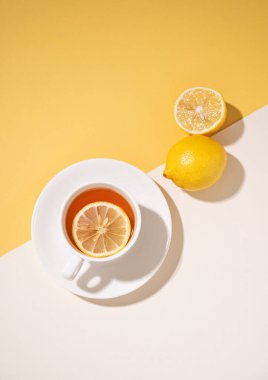 Beyaz ve sarı arka planda gölgeli limonlu bir fincan çay. Sağlıklı ve detoks içeceği konsepti. Üst görünüm ve kopyalama alanı.