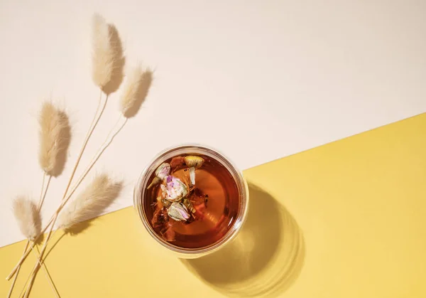 白と黄色の背景に影と花や果物とハーブティーのガラスカップの創造的なレイアウト 健康的な飲み物の概念 トップ表示とコピースペース — ストック写真