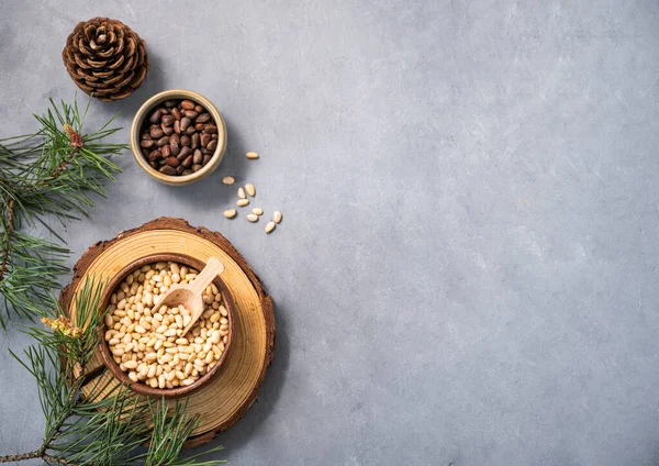 stock image Pine nuts in a bowl and wooden scoop on a blue texture background with branches of pine needles and a cone. The concept of a natural, organic and healthy superfood and snack. Top view and copy space.