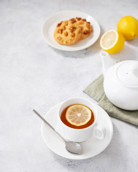 stock image A cup of herbal tea with lemon, cookies and teapot on a light  background. Healthy and detox drink concept. Free space for text.