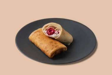 Süzme peynirli ve ahududulu leziz krepler izole bir arka planda koyu bir tabakta yuvarlanıyor. Kahvaltı için sağlıklı ev yemeği kavramı. Metin için boş alan.