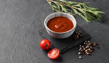 Koyu arkaplanda biber ve biberiyeli bir kasede el yapımı domates sosu. Ev yapımı sağlıklı yemekleri hesaba katın. Metin için boş alan.