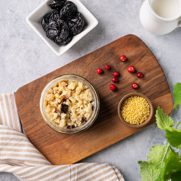 Millet porridge with prunes and fresh berry in a jar on a light background. The concept of a delicious, nutritious and healthy breakfast. Dietary and energy food. Top view.