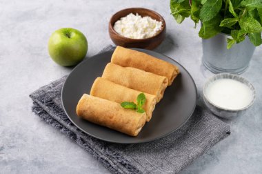 Ekşi krema ve naneli mavi bir arka planda süzme peynirli ve elmalı ev yapımı krep rulosu. Kahvaltı için sağlıklı yemek..