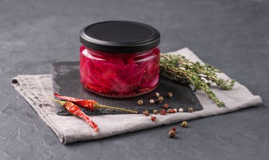 Kavanozda kırmızı soğan halkaları turşusu ve koyu arkaplanda taze otlar. Sağlıklı mayalanmış ev yapımı yiyecekler. 