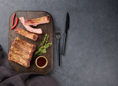 Izgara domuz kaburgası, bbq sosu, acı biber ve ahşap bir tahta üzerinde taze bitki. Üst görünüm ve kopyalama alanı.