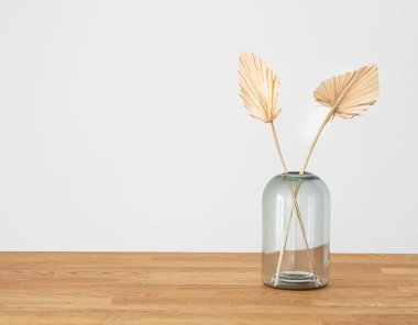 İskandinav tarzında ahşap bir arka planda cam vazoda modern kuru palmiye yaprakları. Art deco, yıldönümü için boho hediyesi, doğum günü, anneler günü. Metin için boş alan.