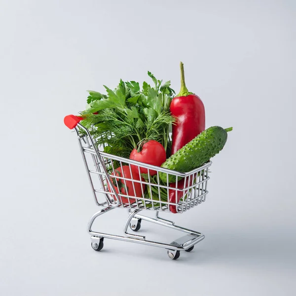 Grocery cart with vegetables and fresh herbs on a blue isolated background. The concept of vegan healthy products. Free space for text.