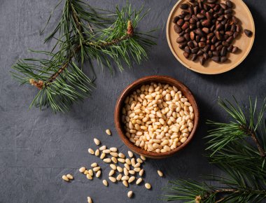 Bir kasede çam fıstığı ve arka planda bir çam iğnesi dalları. Doğal, organik ve sağlıklı abur cubur kavramı. Üst görünüm.