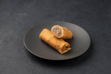 Koyu izole bir arka planda, tabakta tavuk eti olan lezzetli krepler yuvarlanıyor. Kahvaltı için sağlıklı ev yemeği kavramı. Metin için boş alan.