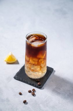 Buzlu ve limonlu uzun bardakta, kahve çekirdekleri ve meyveli açık mavi arka planda, tonik ile soğuk kahve. Moda yazlık ferahlatıcı içecek. Üst görünüm ve kopyalama alanı.
