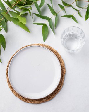 Masa seti, mavi bir tabak ve arka planda okaliptüs dalları olan kamış peçeteye konmuş bir bardak. Çatal bıçakla bahar konsepti. Üst görünüm ve kopyalama alanı.