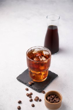 Hafif arka planda buzlu, kahve çekirdekli ve şişeli soğuk bir bardak kahve. Yaz gemisinin ferahlatıcı ev yapımı içeceği. Metin için boş alan.