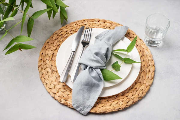 stock image Festive table setting with white plates and glass for a spring celebration, wedding, birthday or mother's day with eucalyptus branches on a light background. Restaurant menu concept. 