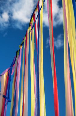 Çok renkli kurdeleler ya da çelenkler, güneşli bir yaz gününde bulutlu mavi gökyüzü ile rüzgarda sallanır. Dini törenler için şenlikli bir dekorasyon konsepti. Yoga festivaline geri çekilin..