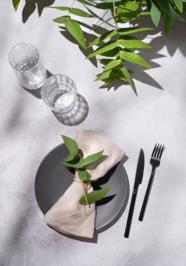 Karanlık gri tabağı ve gölgeli açık arkaplanda okaliptüs dalları olan bir kutlama için gözlüklü şenlik masası. Restoran menüsü konsepti. Üst görünüm ve kopyalama alanı.