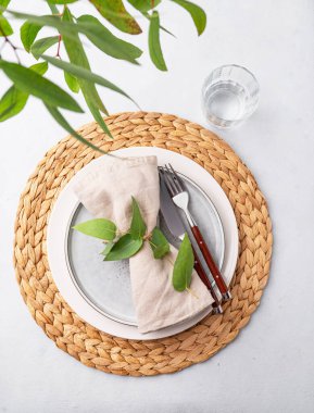 Masa seti, mavi bir tabak ve arka planda okaliptüs dalları olan kamış peçeteye konmuş bir bardak. Çatal bıçakla bahar konsepti. Üst görünüm ve kopyalama alanı.