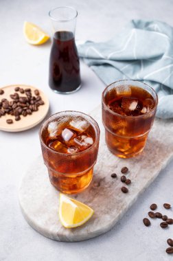 Kahve çekirdekleri, şişeler ve peçetelerle dolu açık arkaplanlı misket tahtasında, limon ve buzlu soğuk bir kahve. Yaz gemisinin ferahlatıcı ev yapımı içeceği. 