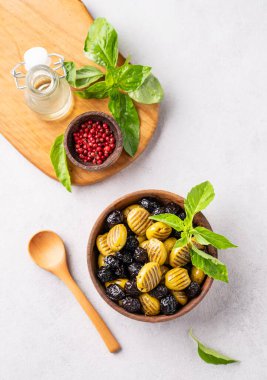 Hafif arka planda zeytinyağı ve fesleğenli ahşap kasede kurutulmuş yeşil ve siyah zeytin seti. Vejetaryen sağlıklı atıştırmalıklar konsepti. Üst görünüm.