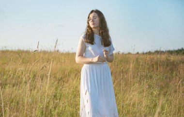 Gözlüklü genç bir kadın ve beyaz bir yaz elbisesi gün batımında çiçeklerle dolu bir tarlada..