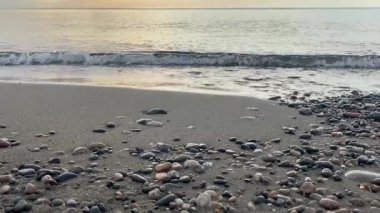 Sahilde gün batımında çakıl taşları ve taşlarla deniz dalgaları. Bir yaz akşamında Karadeniz kıyısında. Gürcistan, Batum. 