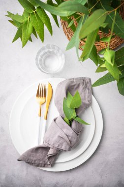 Peçete ve okaliptüs dallı hafif arka planda beyaz tabaklar ve çatal bıçak takımlarıyla şenlik masası. Restoran menüsü konsepti. Üst görünüm 