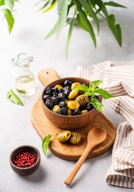 Hafif arka planda zeytinyağı ve fesleğenli ahşap kasede kurutulmuş yeşil ve siyah zeytin seti. Vejetaryen sağlıklı atıştırmalıklar konsepti. 