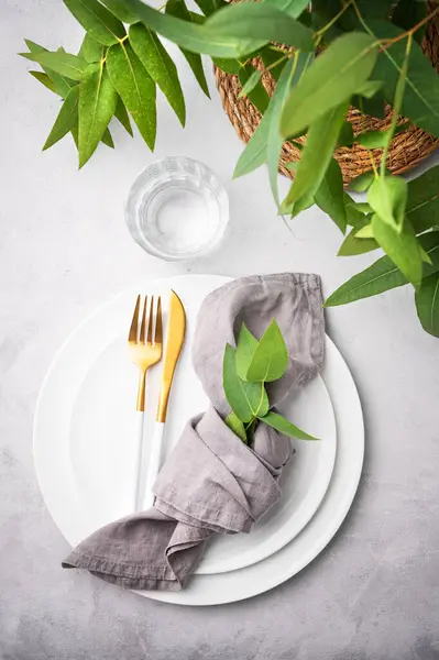 Peçete ve okaliptüs dallı hafif arka planda beyaz tabaklar ve çatal bıçak takımlarıyla şenlik masası. Restoran menüsü konsepti. Üst görünüm 