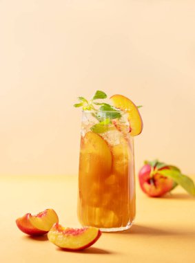 Şeftalili buz ve nane çayı. Vejetaryen ev yapımı soğuk yaz içeceği turuncu arka planda, uzun bardakta ve taze meyveli. Metin için boş alan.
