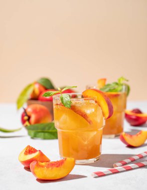 İki bardak şeftalili çay, buzlu ve naneli. Hafif arka planda taze meyve ve gölgeli ev yapımı soğuk yaz içeceği. Ön görünüm ve boşluk kopyala.