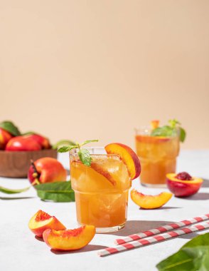 İki bardak şeftalili çay, buzlu ve naneli. Hafif arka planda taze meyve ve gölgeli vejetaryen ve ev yapımı soğuk bir içecek. Ön görünüm ve boşluk kopyala.