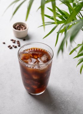 Hafif arka planda kahve çekirdekleri ve palmiye yaprağıyla birlikte buzlu kahve bardağında demlenmiş. Yaz ferahlatıcı içecek konsepti. Üst görünüm.