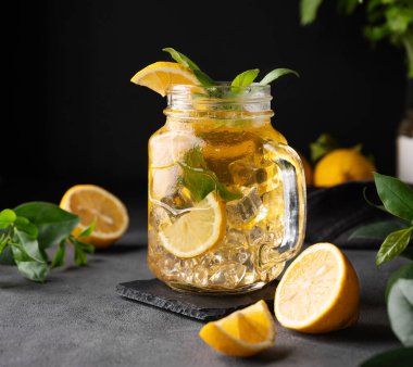 Limonata, taze limon, naneli ve buzlu bir kavanozda. Limonlu mojito kokteyli ya da koyu bir arka planda soğuk çay. Ev yapımı sağlıklı ve detoks içeceği konsepti. Ön görünüm.