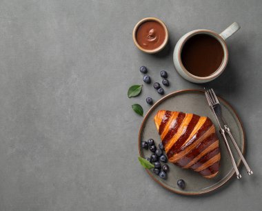 Çikolatalı ve yaban mersinli taze kruvasan yeşil arka planda koyu bir tabakta ve bir fincan sade kahveyle. Köy tarzında nefis ev yapımı kahvaltı konsepti. Üst görünüm ve kopyalama alanı.