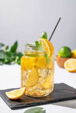 Limonata ya da taze limon, nane ve buzlu soğuk çay. Taze meyve ve gölgelerle siyah tahtada narenciye kokteyli serinletiyorum. Ön görünüm.