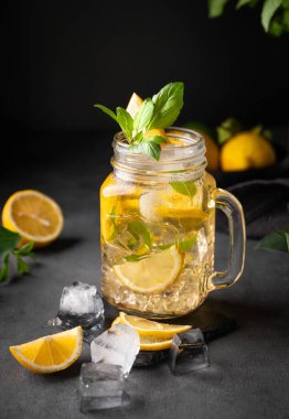 Limonata, taze limon, naneli ve buzlu bir kavanozda. Limonlu mojito kokteyli ya da koyu bir arka planda soğuk çay. Ev yapımı sağlıklı ve detoks içeceği konsepti. Ön görünüm.