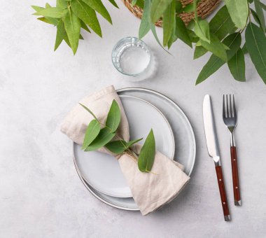 Okaliptüs dallı hafif bir arka planda kutlama için iki tabak ve cam ile şenlik masası. Restoran menüsü konsepti. Üst görünüm ve kopyalama alanı.