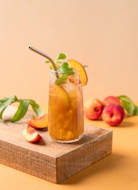 Şeftalili buz ve nane çayı. Turuncu arka planda uzun bardakta taze meyveli ev yapımı soğuk yaz içeceği. Metin için boş alan.