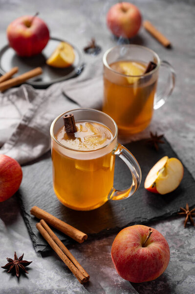 Homemade apple punch with fresh apples, cinnamon and spices in cups on dark background with fresh fruits. A hot, healthy autumn or winter drink. The concept of a homely cozy atmosphere.