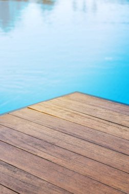 Mavi kiremitli bir yüzme havuzunun önündeki boş ahşap masa. Yaz arkaplanlı ürün sunumu konsepti. Metin için boş alan.
