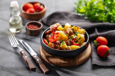 Patates, soğan ve biberli kızarmış domuz eti. Ulusal ev yapımı Gürcistan yemeği siyah bir tavada, arka planda taze otlar, baharatlar ve domateslerle birlikte..